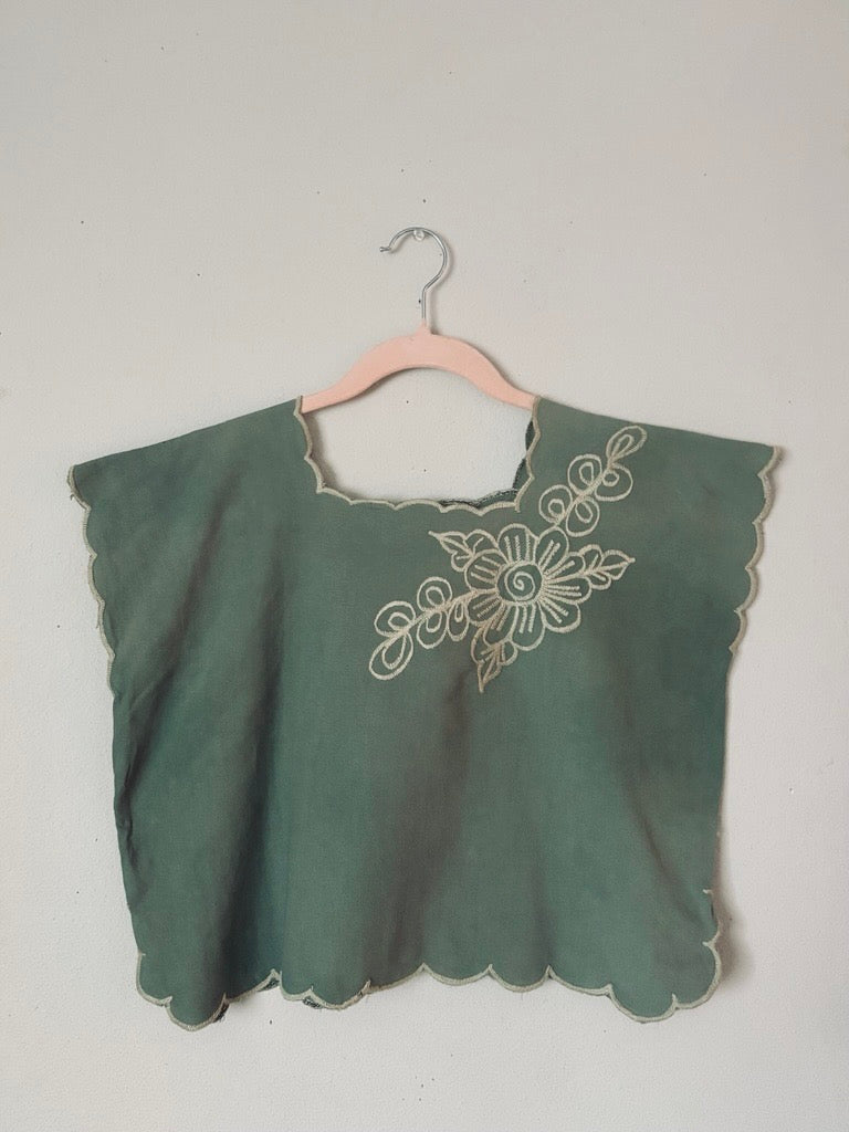 Mexican Green blouse with white embroidery on a hanger against a plain background