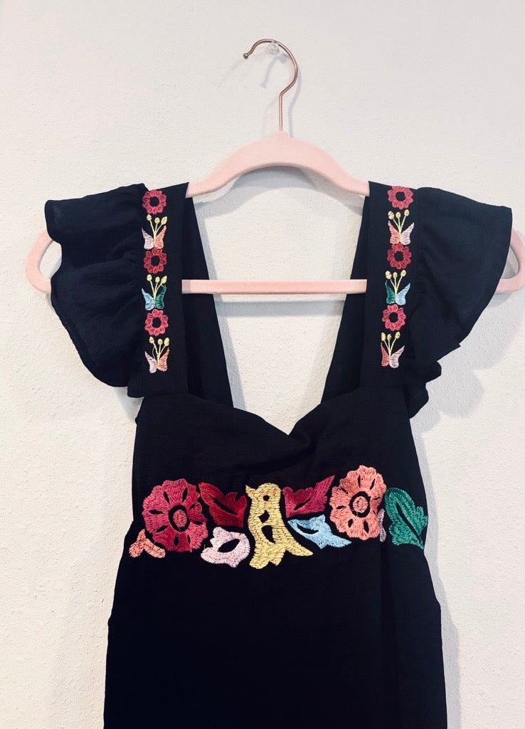 Mexican Black dress with colorful floral embroidery on a hanger against a white background